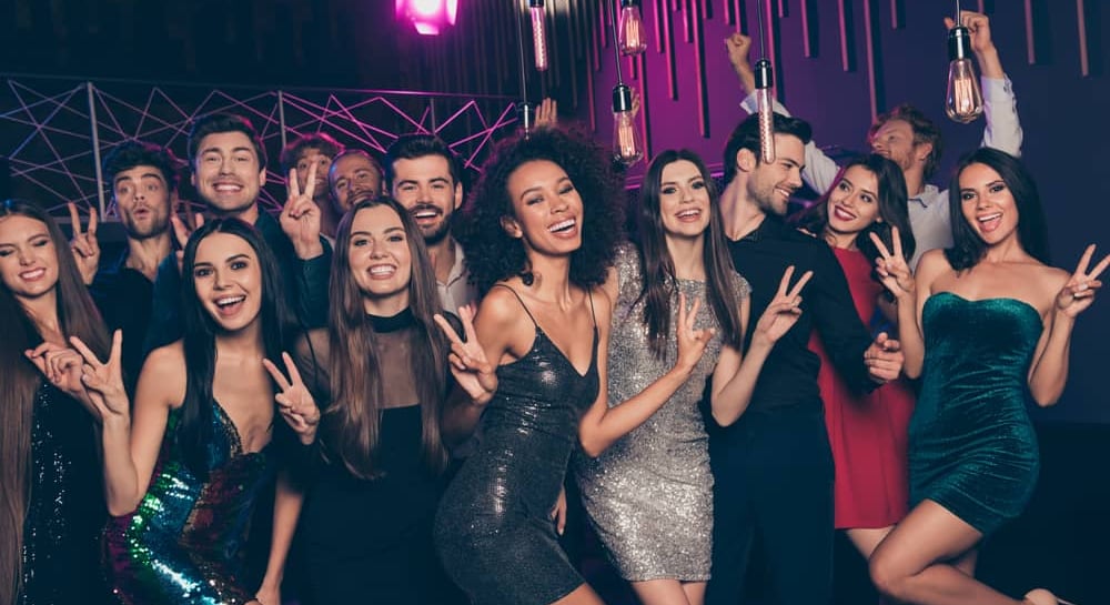 Large group of friends enjoying a night out at a Las Vegas club crawl, smiling and making peace signs during the lively party