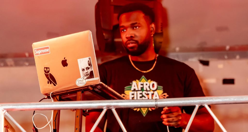 A DJ performing at the Afro Fiesta Festival under red stage lights with a laptop and turntable.