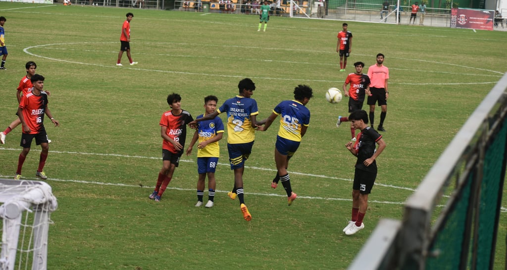 A group of teenage boys playing a competitive soccer match on a green field at a stadium.