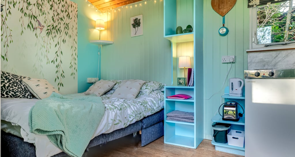 Cozy mint green garden room interior with a double bed, wood paneled ceiling, and turquoise shelving.