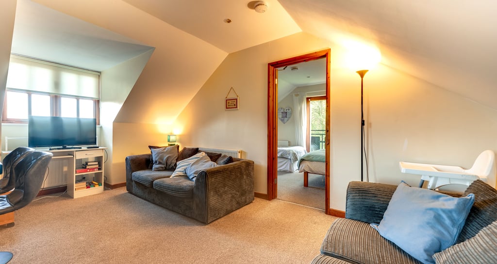 Cozy attic living room with grey corduroy sofas, television, and doorway leading to a bright bedroom.