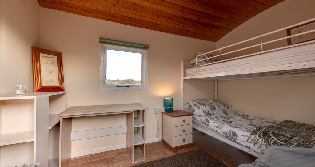 Small bedroom featuring a white bunk bed, wooden ceiling, and a desk under a window.