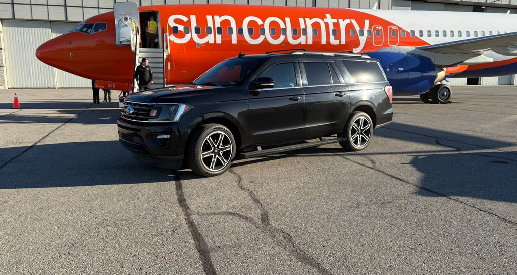 a black suv parked in front of a sun country air plane