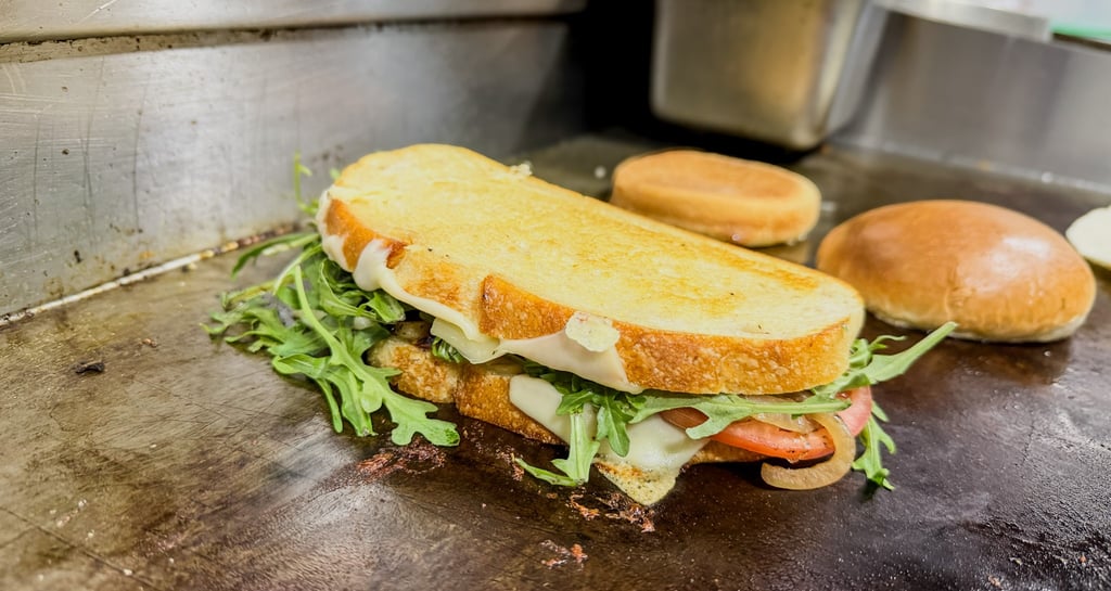 A gourmet panini with melted cheese, fresh arugula, and tomato on a flat top grill.