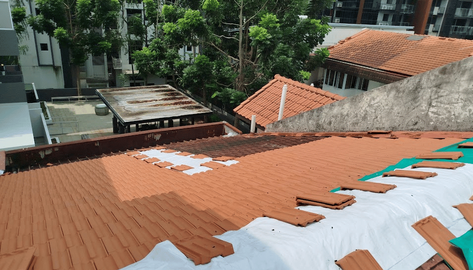 Roofer installing new terracotta roof tiles over a white waterproof membrane on a residential building.