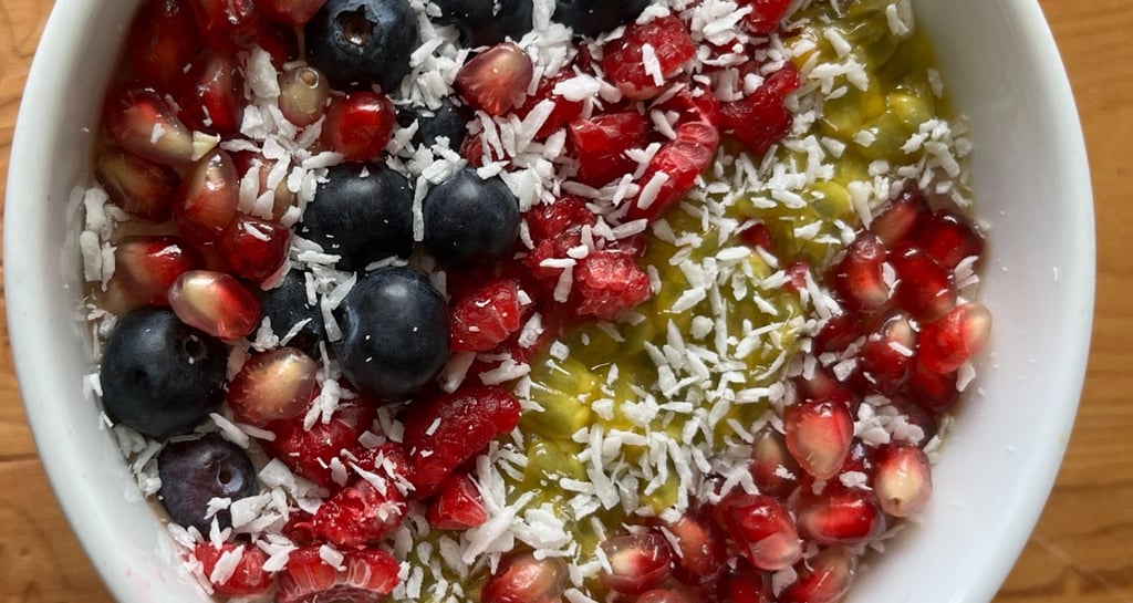 A healthy breakfast bowl topped with blueberries, pomegranate seeds, shredded coconut, and kiwi fruit.