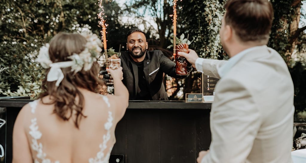 Professional mobile bartender serving tiki cocktails with sparklers to a bride and groom at an outdoor wedding.