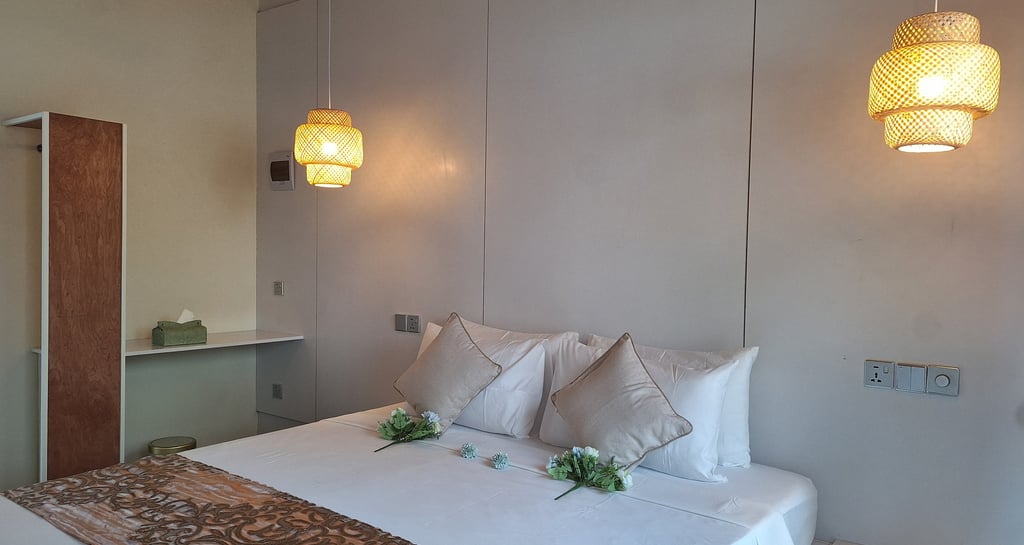 Modern hotel bedroom with white linens, decorative pillows, and warm woven pendant lights.