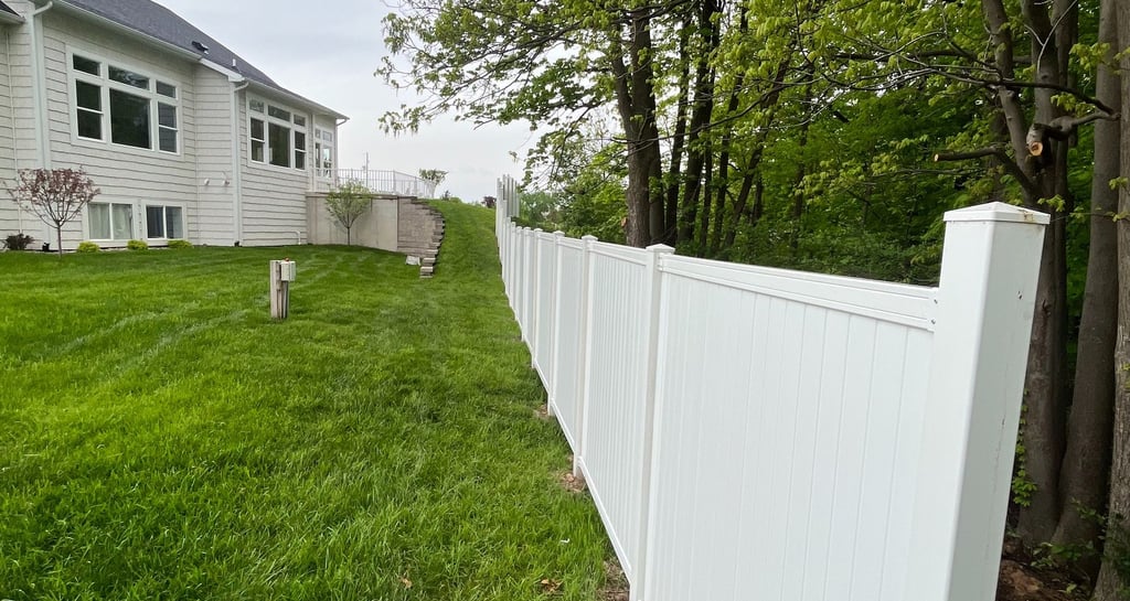 White vinyl privacy fence installed in a green backyard bordering a wooded area.