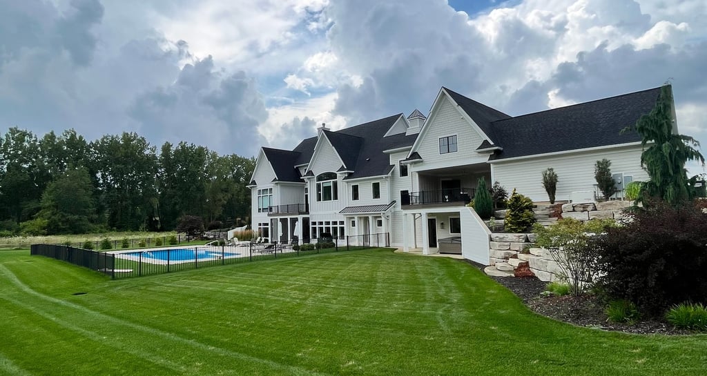 Luxury white modern farmhouse with a swimming pool and manicured green lawn under a cloudy sky.