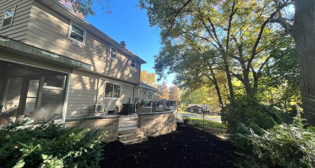 A backyard landscape featuring a stone retaining wall and fresh black mulch under autumn trees.