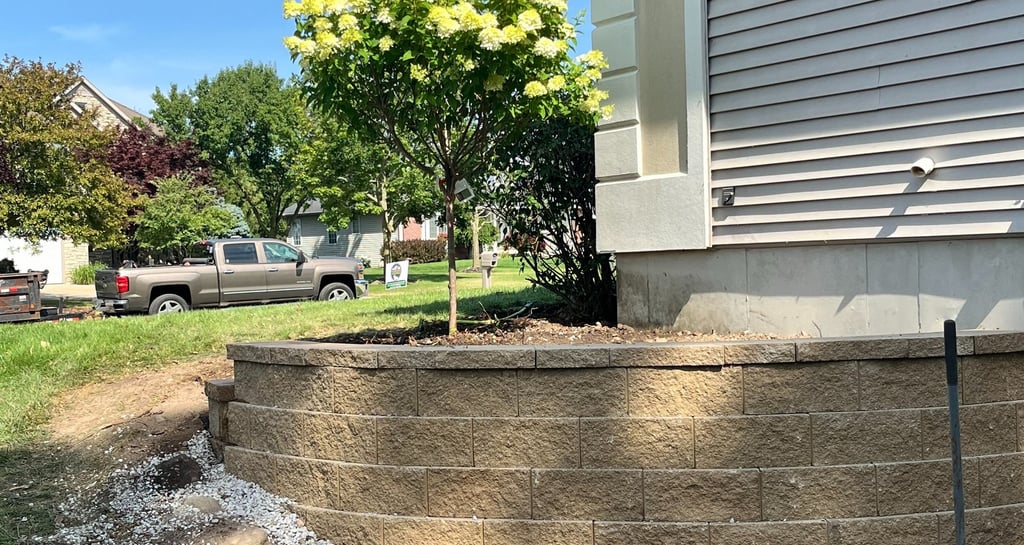 New stone retaining wall in front of a house with a flowering hydrangea tree and landscaping.