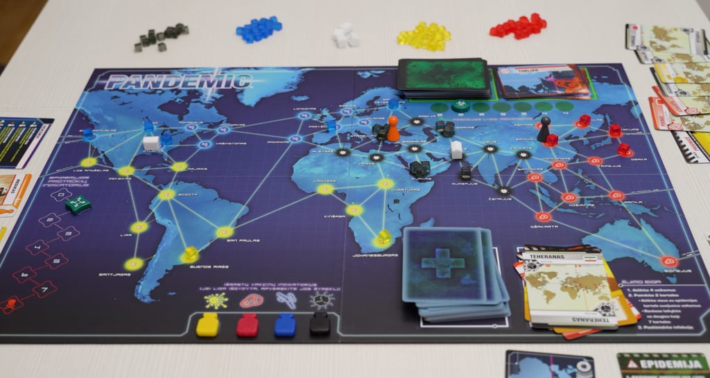 Stalo žaidimo lenta ant kurios sudėtos kortos, ligų kubeliai ir žaidėjų vaikštukai