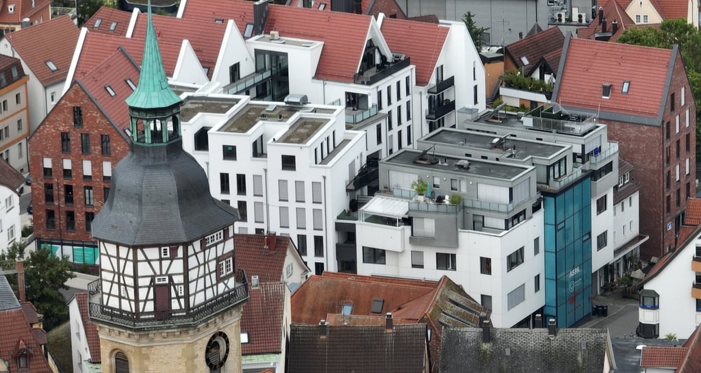 Aerial view of a German old town featuring a historic church tower and modern white apartments with red tile roofs.