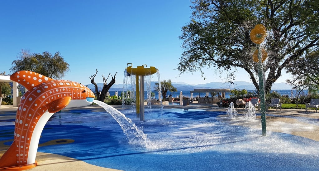 Outdoor kids splash pad with a whale fountain and water spray features at a sunny luxury resort.