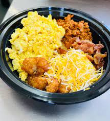 Breakfast bowl with scrambled eggs, country potatoes, shredded cheese, and crispy bacon.