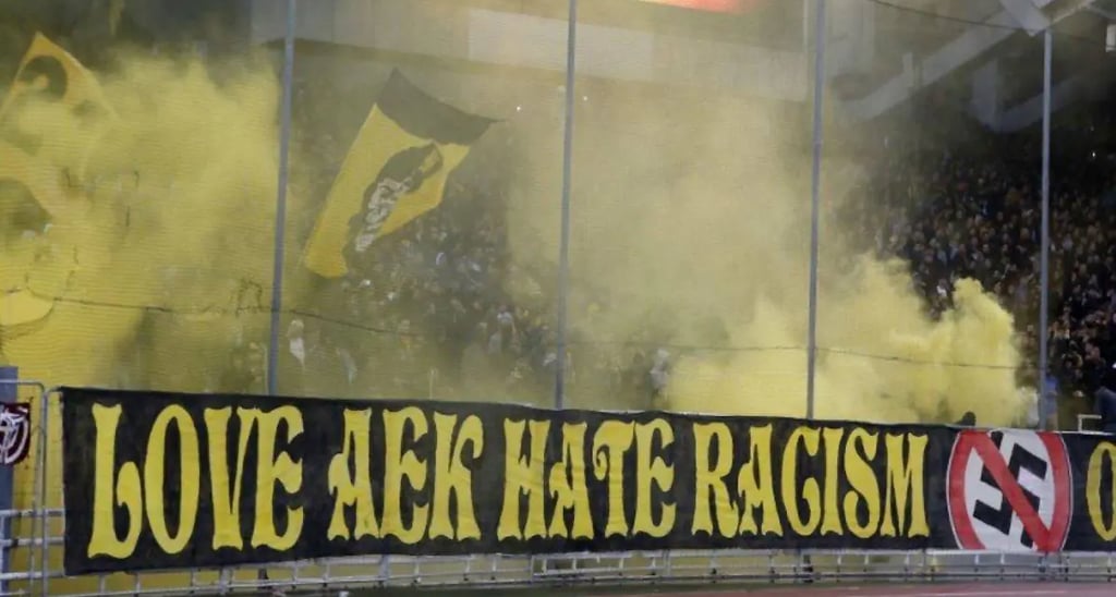 Leidenschaftliche AEK-Athen-Fans in gelb-schwarzen Farben mit Fahnen und Pyrotechnik auf den Rängen des Agia-Sofia-Stadions.
