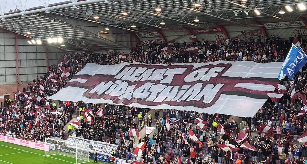 Innenansicht des Tynecastle Park in Edinburgh: dicht gefüllte Tribünen mit jubelnden Fans, rot-weißen Vereinsfarben, klar erk