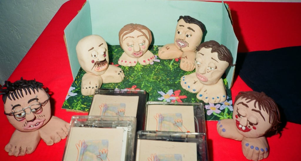 Handmade clay figurines of heads on feet displayed with cassette tapes on a red surface.