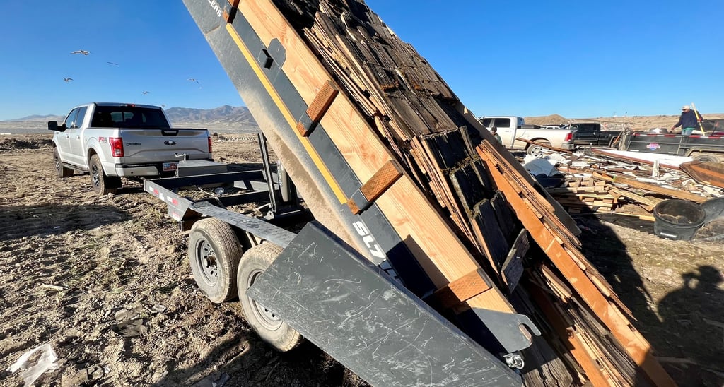 a truck with a dump trailer extended up, dumping a load of roofing debris 