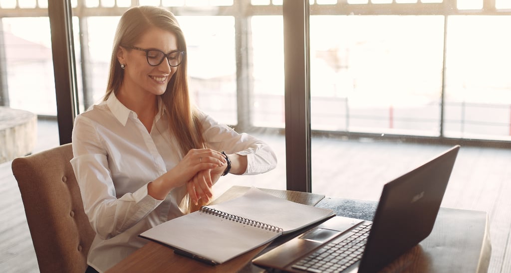 a woman sitting on her desk with a laptop and watching her time to indicate time management