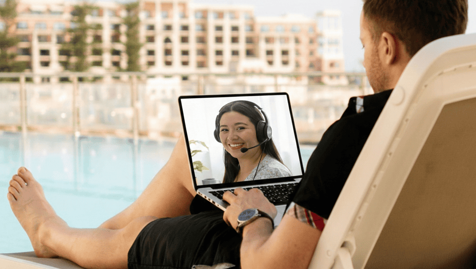 student in front of a pool resort in the backround while holding a computer with the face the tutor from Hola with Alo