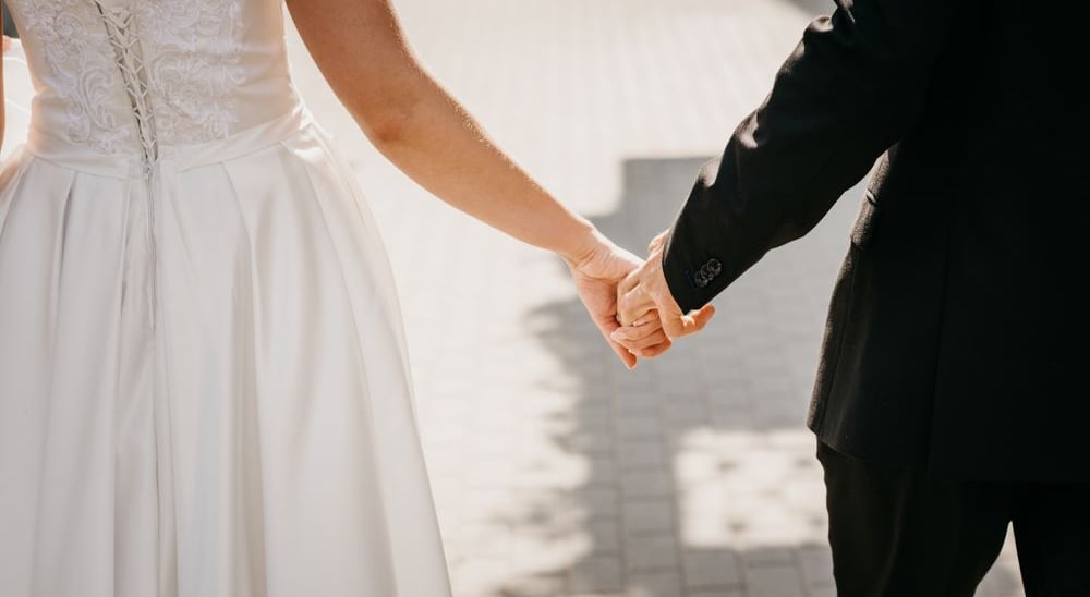 a bride and groom holding hands and walking down a path