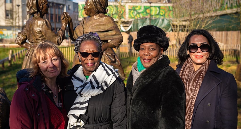 a group of women standing in front of a statue of a man