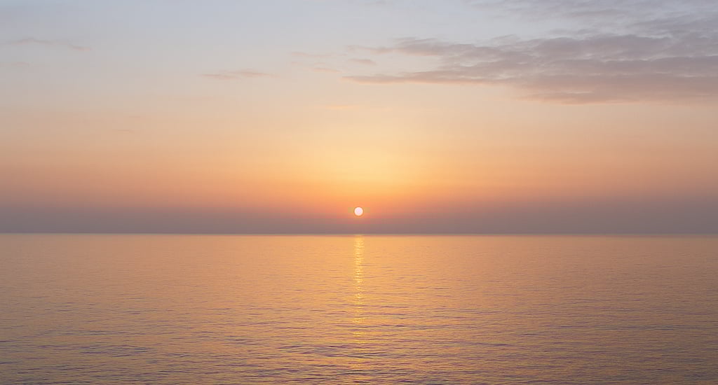 A soft sunrise over a calm sea, the sky shifting from darkness to light 