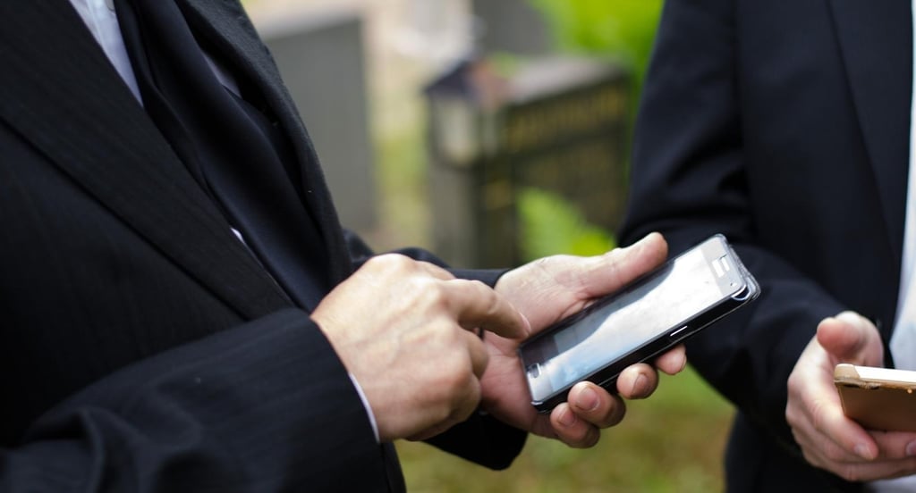 two men in suits and ties are holding their phones - Illford Academy