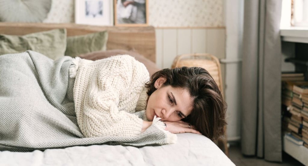 Tired woman lying in bed wearing a knit sweater, looking depressed and lonely at home.
