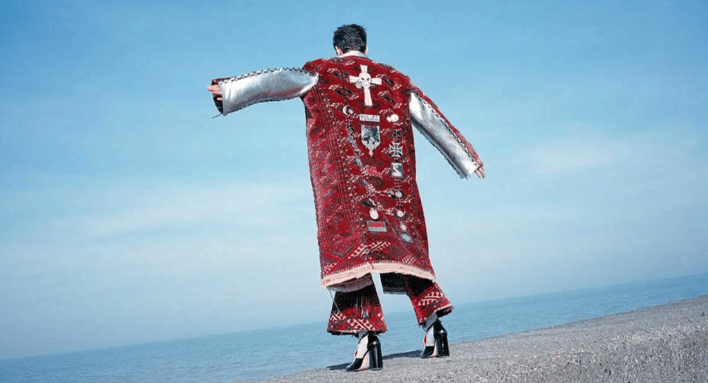 Back view of couture red embroidered coat styled against coastal backdrop.