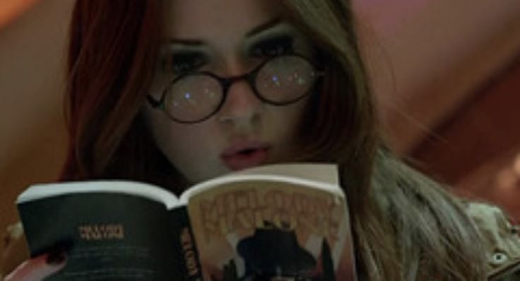 a woman in glasses and a jacket is reading a book