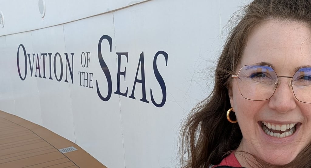 A woman smiling by the side of a Royal Caribbean ship that says Ovation of the Seas