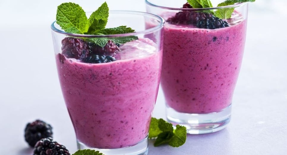 Two glasses with purple smoothie inside, mint leaves and blackberries garnish