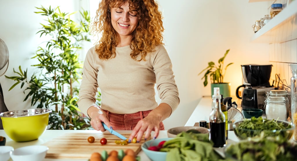 Smiling woman chopping vegetables in a bright kitchen with plants and fresh produce