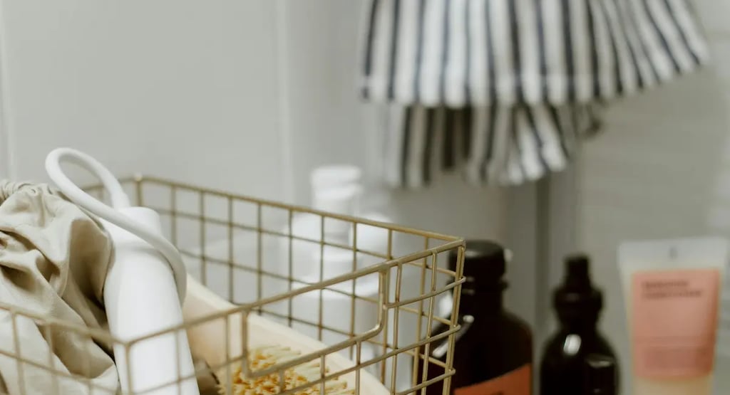 A white hair dryer and body brush in a wire storage basket on a wooden bathroom counter.