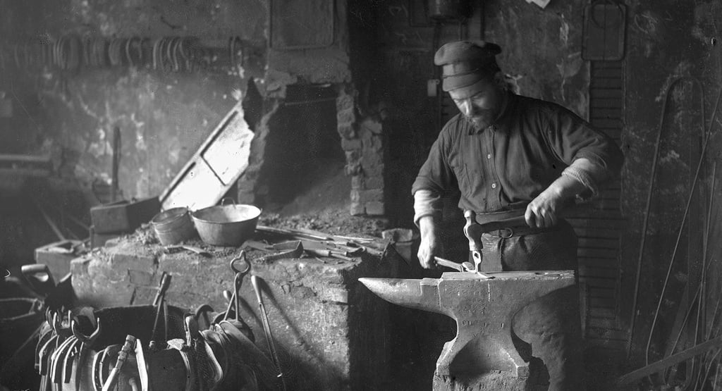 Vintage black and white photo of a blacksmith forging metal on an iron anvil in a traditional forge.