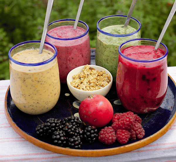 four smoothie glasses in tray with some fruits