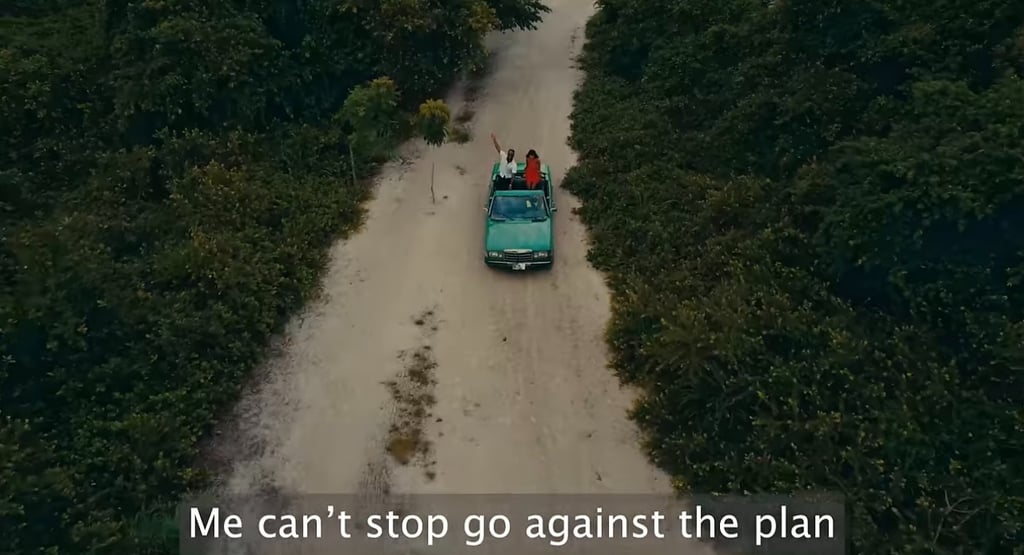 a aqua green car driving down a dirt road with 2 people on it with shrubbery bush on the sides