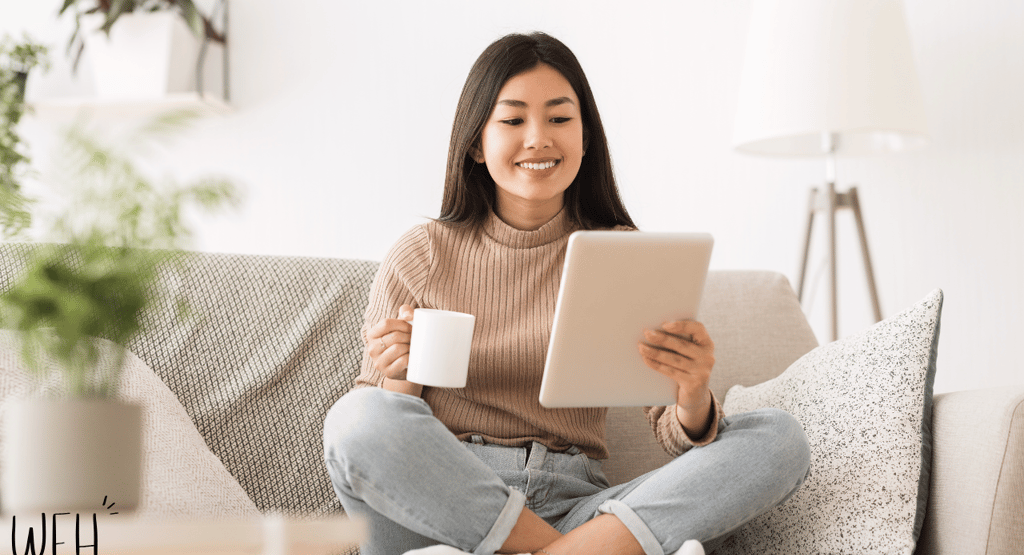 a woman sitting on a couch holding a cup of coffee and a tablet