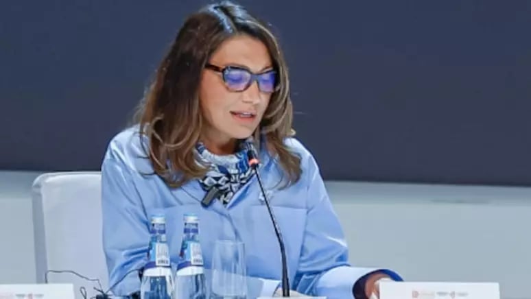 a woman in a blue shirt and glasses sitting at a table