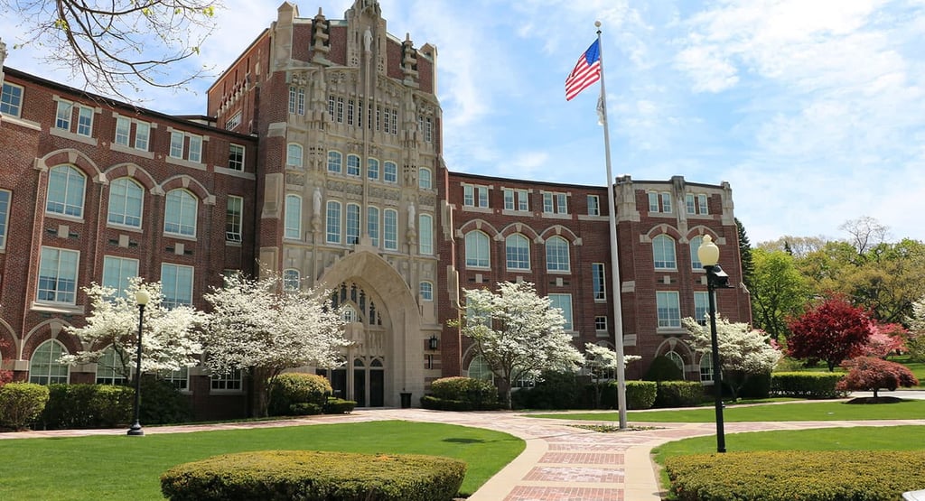 Grand brick building at Providence College with archway, blossoming trees, and American flag