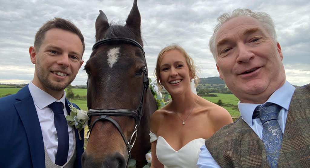 a bride and groom posing for a photo with a horse and celebrant