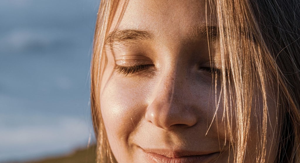Moters veidas užmerktomis akimis, besišypsantis, apšviestas saulės, laimės ir ramybės akimirka