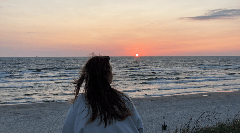 a woman standing on a beach with a sunset in the background