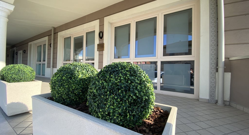 Two round artificial topiary boxwood balls in a large concrete planter outside a modern office building.