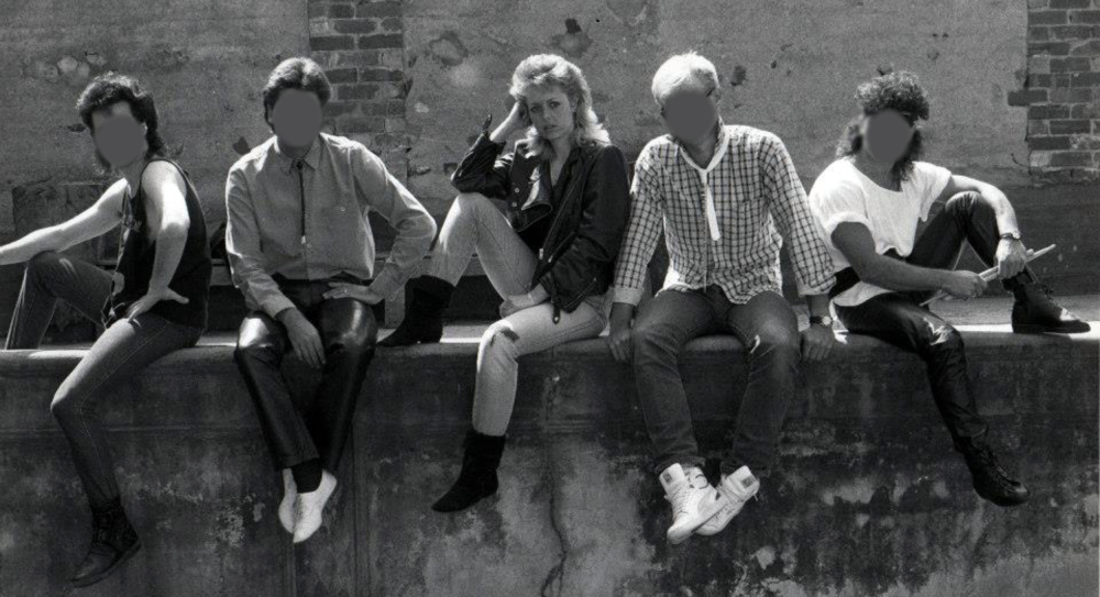 Black and white image of a young woman sitting on a wall with her four male band mates