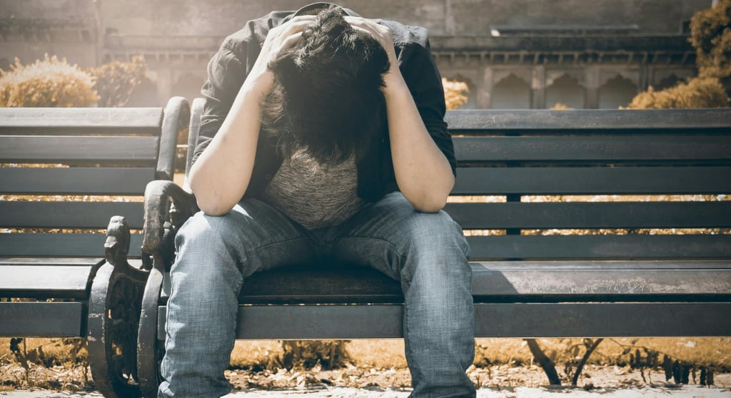 Vyras sėdintis parke ant suoliuko su nusileista galva, apimtas nerimo.