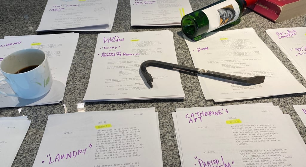 Multiple piles of play script on a table, with a coffe cup, empty wine bottle & crowbar on top